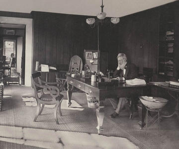 Sepia-toned photograph of Asa Gray seated at a large wooden desk in a room with paneled walls and scattered papers, circa 1875