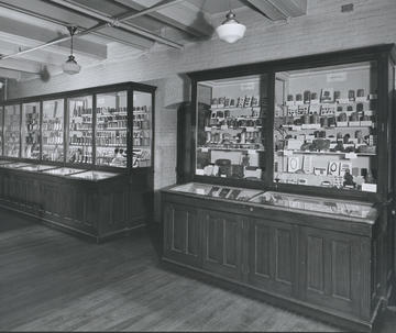 "Black-and-white photograph of the Economic Botany display at the University Museum, circa 1900, showing multiple glass display cases filled with labeled botanical specimens and teaching materials