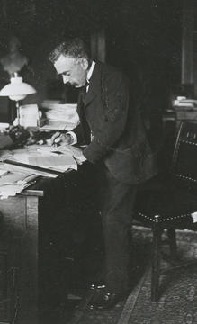 Black-and-white photograph of William Gilson Farlow standing beside a desk covered with papers and books in his office, dated 1873